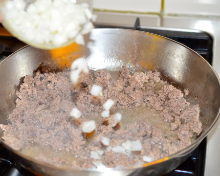 adding chopped onions to cooking ground beef