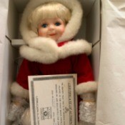 Value of a Dynasty Porcelain Doll - doll in box wearing a red coat with white fur trim