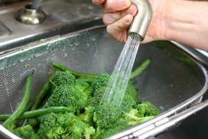 A sink sprayer being used to rinse broccoli.