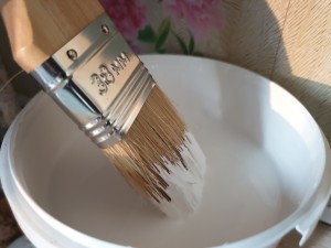 A paintbrush in a bucket of white paint.
