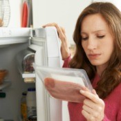 A woman looking at a package of meat from the fridge.