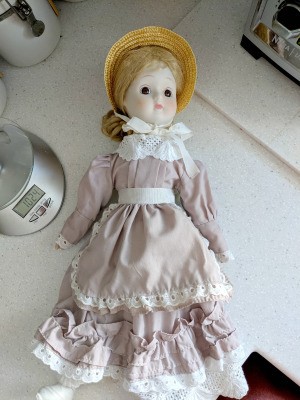 Identifying a Porcelain Doll - doll wearing a straw bonnet, and a dusty rose colored long dress with eyelet trim
