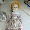 Identifying a Porcelain Doll - doll wearing a straw bonnet, and a dusty rose colored long dress with eyelet trim