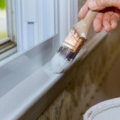 A paintbrush being used to paint a white windowsill.