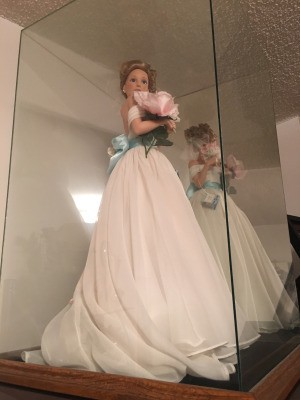 Value of an Ashton Drake Doll - doll wearing a long white dress with a blue sash in a clear doll display case