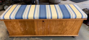Value of a Lane Cedar Chest - medium wood finish chest with blue, black, white, and yellow striped cushion