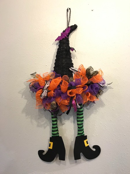 A witch hat decorated with ribbons and striped witch legs, as a Halloween decoration.