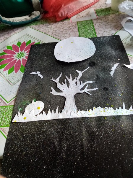 Halloween Toothbrush Spray Painting - moon covered with a circle of paper and other element cutouts arranged on black paper