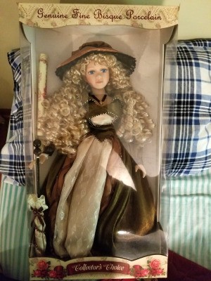 Value of a Collector's Choice Porcelain Doll - blond doll with very long ringlets, wearing a brown and cream dress and holding perhaps a twig broom