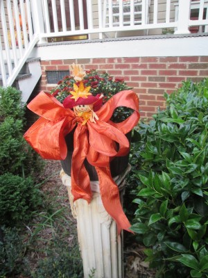 Dressing Up Your Garden With Ribbon - potted mums on white column pedestal decorated with orange ribbon and small figure tuck in bow