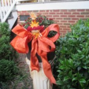 Dressing Up Your Garden With Ribbon - potted mums on white column pedestal decorated with orange ribbon and small figure tuck in bow