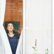 A woman closing curtains in a large window.