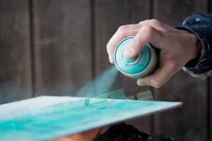 A person using a can of blue-green spray paint.