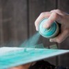A person using a can of blue-green spray paint.