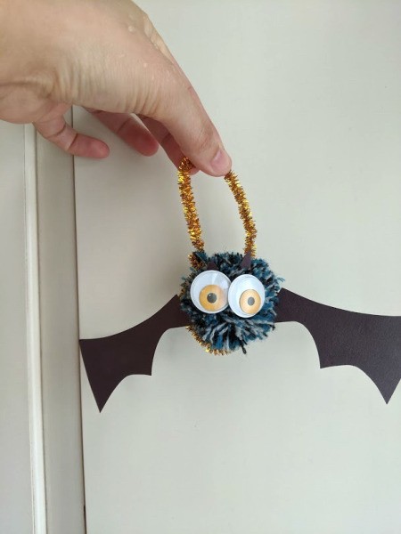 Pom Pom Bat Decoration - hand holding the bat hanging from a gold pipe cleaner