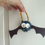 Pom Pom Bat Decoration - hand holding the bat hanging from a gold pipe cleaner