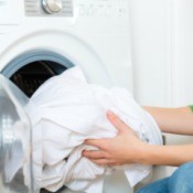 White laundry being loaded in a washing machine.