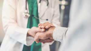 A doctor holding the hand of a patient in comfort.