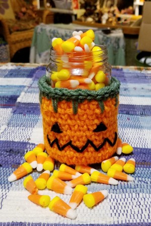 Crocheted Pumpkin Candy Jar Cover - pumpkin candy jar filled with candy corn, with some scattered around the jar on the table