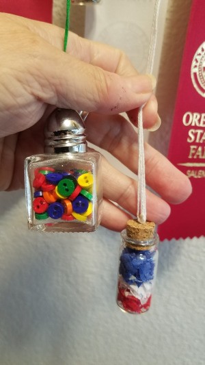 Two tiny hanging glass jars filled with beads or buttons.