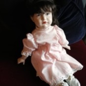 Value of a Reproduction Kammer & Reinhardt Porcelain Doll - dark haired doll wearing a pink dress with eyelet lace trim