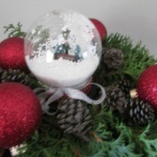 Budget Friendly Snow Globe - filled globe surrounded by red Christmas ornaments, pine cones, and greenery