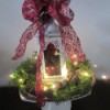 Making A Lantern Part Of Your Holiday Decor - ornament filled white lantern on a display stand surrounded by greenery, pine cones, and fairy lights