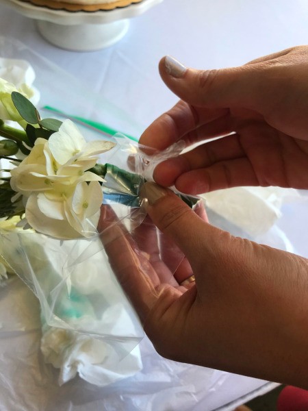 Adding Fresh Flowers to Cake Decoration - closeup of wrapping the stem with a piece of a plastic bag the day of