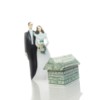 Bride and groom cake topper next to money folded into a house shape.