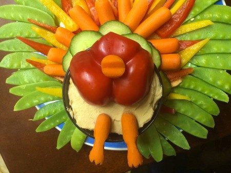 Thanksgiving Turkey Veggie Tray - place red pepper bottom on the bowl of hummus leaving space to add the feet, glue beak in place using a dab of hummus, place the feet at the bottom, partially in the hummus bowl
