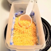 A container containing shredded cheese and a measuring cup used as a scoop.