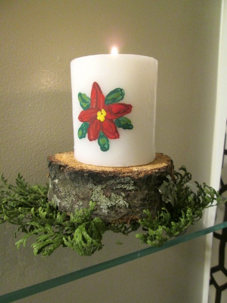Designing Two For One - lit poinsettia candle sitting on a log slice, with greenery in front