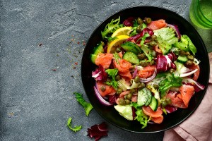 A vegetable and salmon salad in a black bowl.