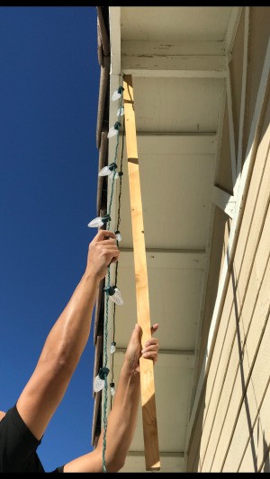 Using a stick to hang Christmas lights on the house.