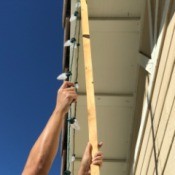 Using a stick to hang Christmas lights on the house.