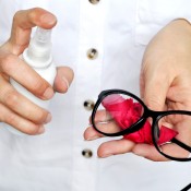 Person spraying their glasses with cleaner.