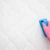 Pink rubber glove with blue brush scrubbing mattress.