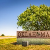 A road sign that states "Oklahoma" next to a tree and sky vista.