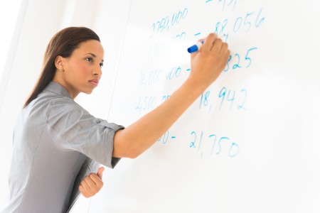 Photo of a teacher writing on a dry erase board with her sleeves rolled up.