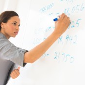 Photo of a teacher writing on a dry erase board with her sleeves rolled up.