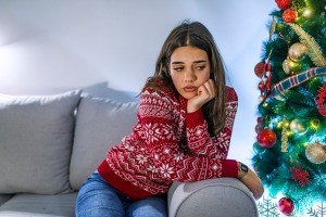 An unhappy young woman sitting on the couch next to a Christmas tree.