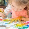 A girl painting her fingers and paper with watercolors.