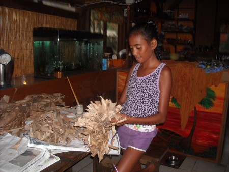 Dried Banana Leaf Crown - girl standing holding the wreath with a pile of dried leaves on a table next to her