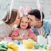 A man, woman and child with bunny ears on, decorating eggs.