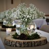 Babysbreath flowers in a fishbowl vase surrounded by pinecones on a round of wood.