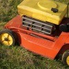 An old lawn mower, painted yellow and orange.