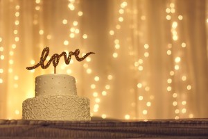White cake with a "love" topper, twinkling light backdrop.