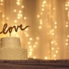 White cake with a "love" topper, twinkling light backdrop.