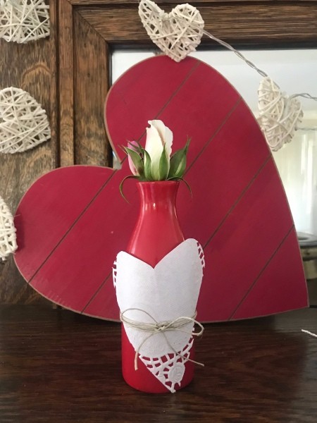 Transform any Vase into a One with a Valentine's Theme - red bottle with heart decoration with a rose bud, in front of a red wood/paper heart