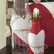 Transform any Vase into a One with a Valentine's Theme - clear bottle and red vase decorated with paper doily hearts